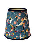 A dark blue paper lampshade with a pink, red and orange marbled design and a navy velvet trim. 